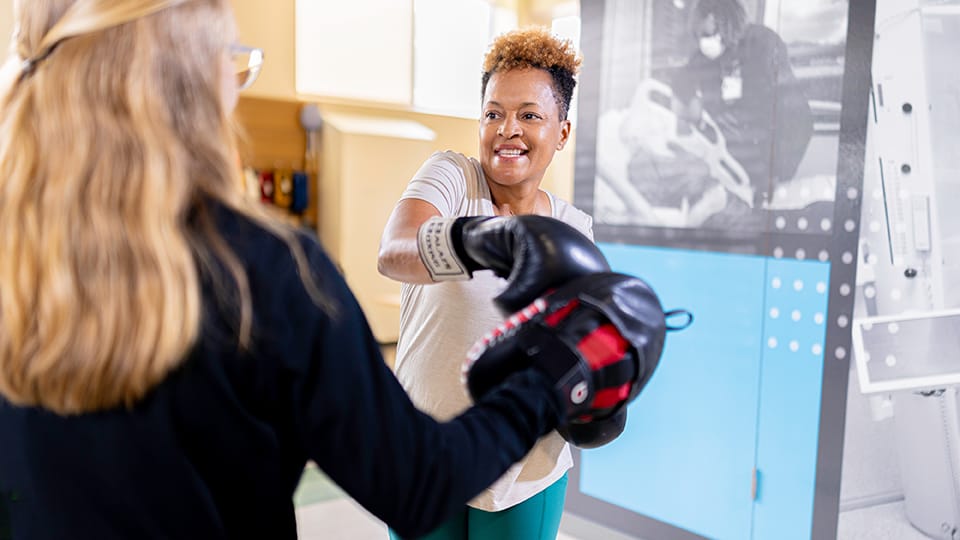 Woman wearing boxing gloves does a work out with a therapist.