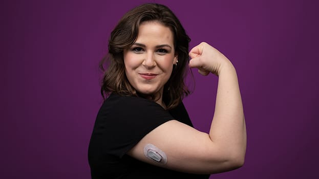 Woman smiling, flexing muscle with a diabetes arm monitor on