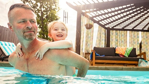 Man with child on his back wading in a swimming pool