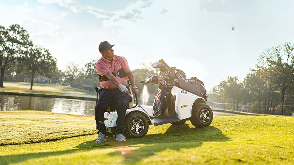 Man who uses a wheelchair hits a ball on the golf course using an adaptive chair.